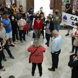 Foto de cima do saguão principal do Paço Municipal cheio dos servidores em volta do secretário adjunto de Gestão que escuta uma diretora do sindicato lendo as reivindicações.