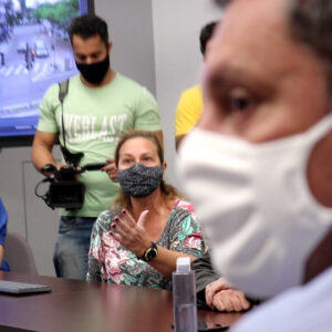 Foto da reunião onde aparece o prefeito em primeiro plano olhando pro lado e uma aposentada no segundo plano falando com ele e gesticulando